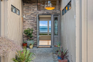 Steps leading up to an open door with plants along the path and a room with large windows visible inside.