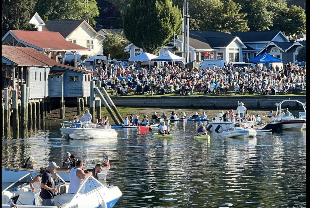 People on boats and a crowd of people on shore at an event.